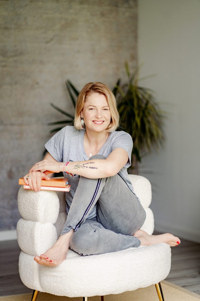 Jane sitting on a white chair in grey jeans and t-shirt